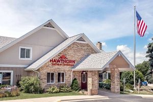 Hawthorn Suites by Wyndham hotel with brick facade, peaked roofs, and an American flag on a tall flagpole to the right.